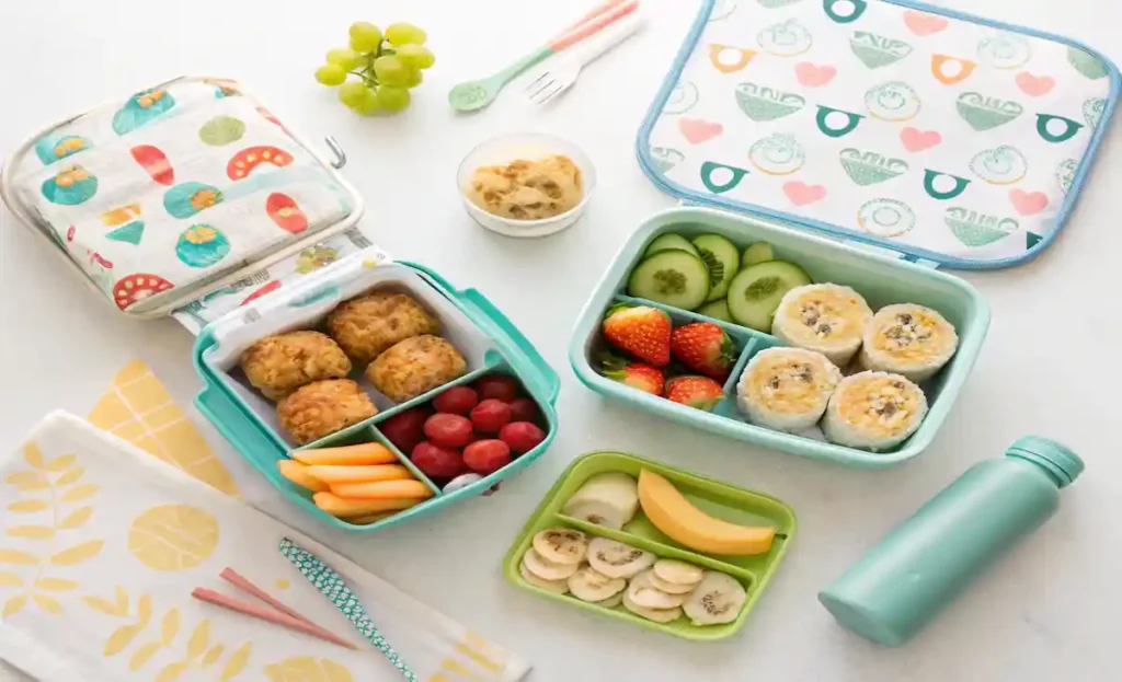 "A fun and balanced toddler lunch display with colorful roll-ups, muffins, fruits, sandwiches, and veggies packed in cute lunchboxes."