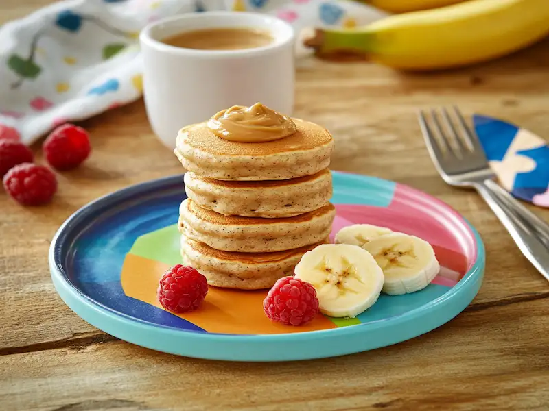 A toddler plate with banana oat pancakes and nut butter drizzle, served with fruit — a wholesome breakfast idea for toddler friendly meals.